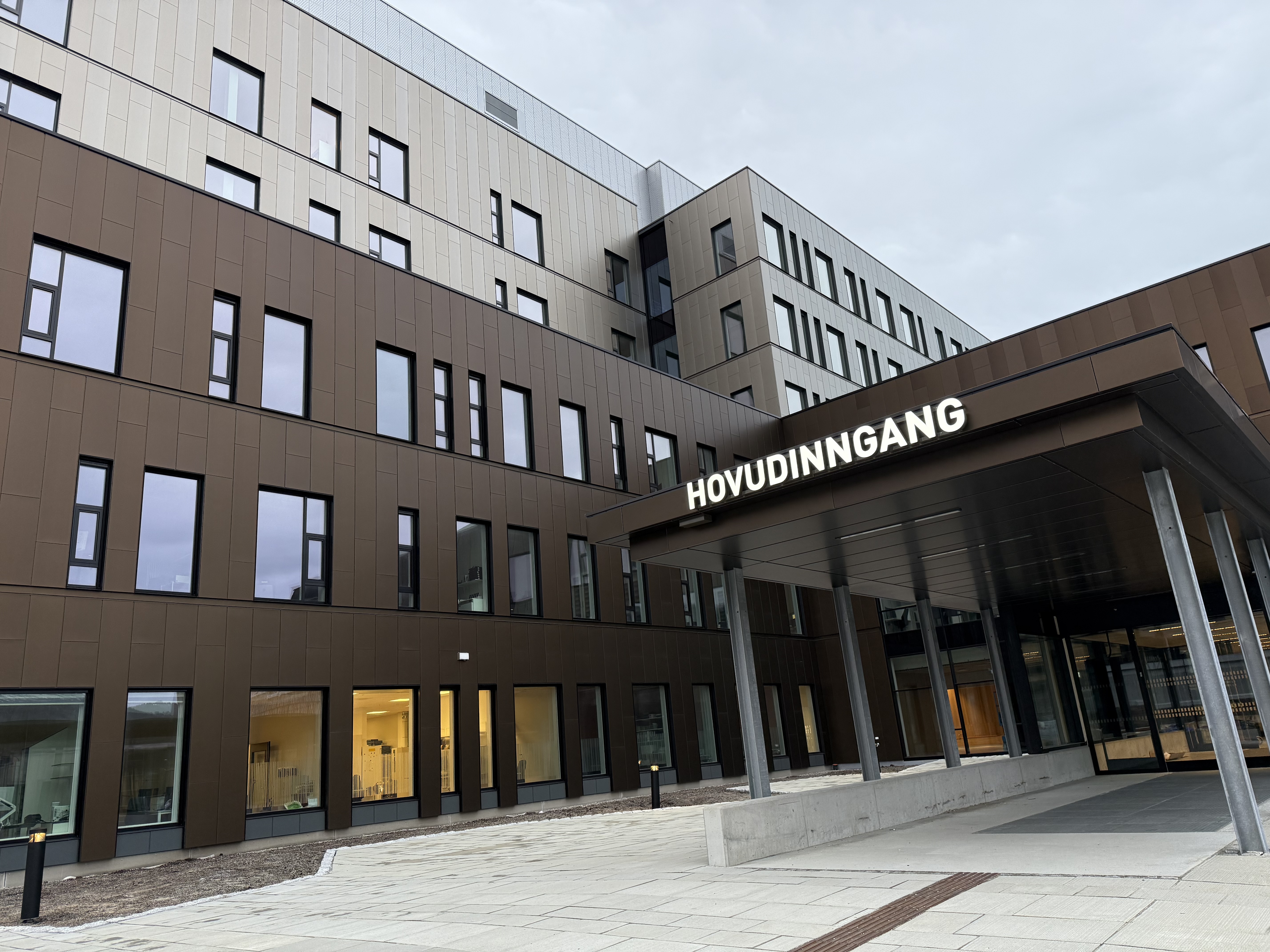 Bildet viser et moderne bygg i flere etasjer med vinduer i forskjellige størrelser. Inngangspartiet er under et takoverbygg med søyler. Over inngangen står teksten Hovudinngang.