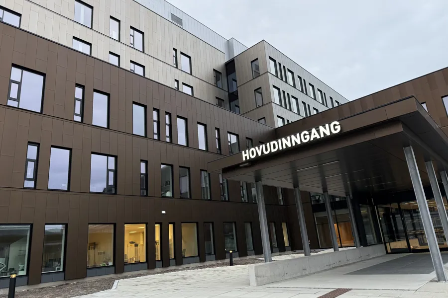 Bildet viser et moderne bygg i flere etasjer med vinduer i forskjellige størrelser. Inngangspartiet er under et takoverbygg med søyler. Over inngangen står teksten Hovudinngang.