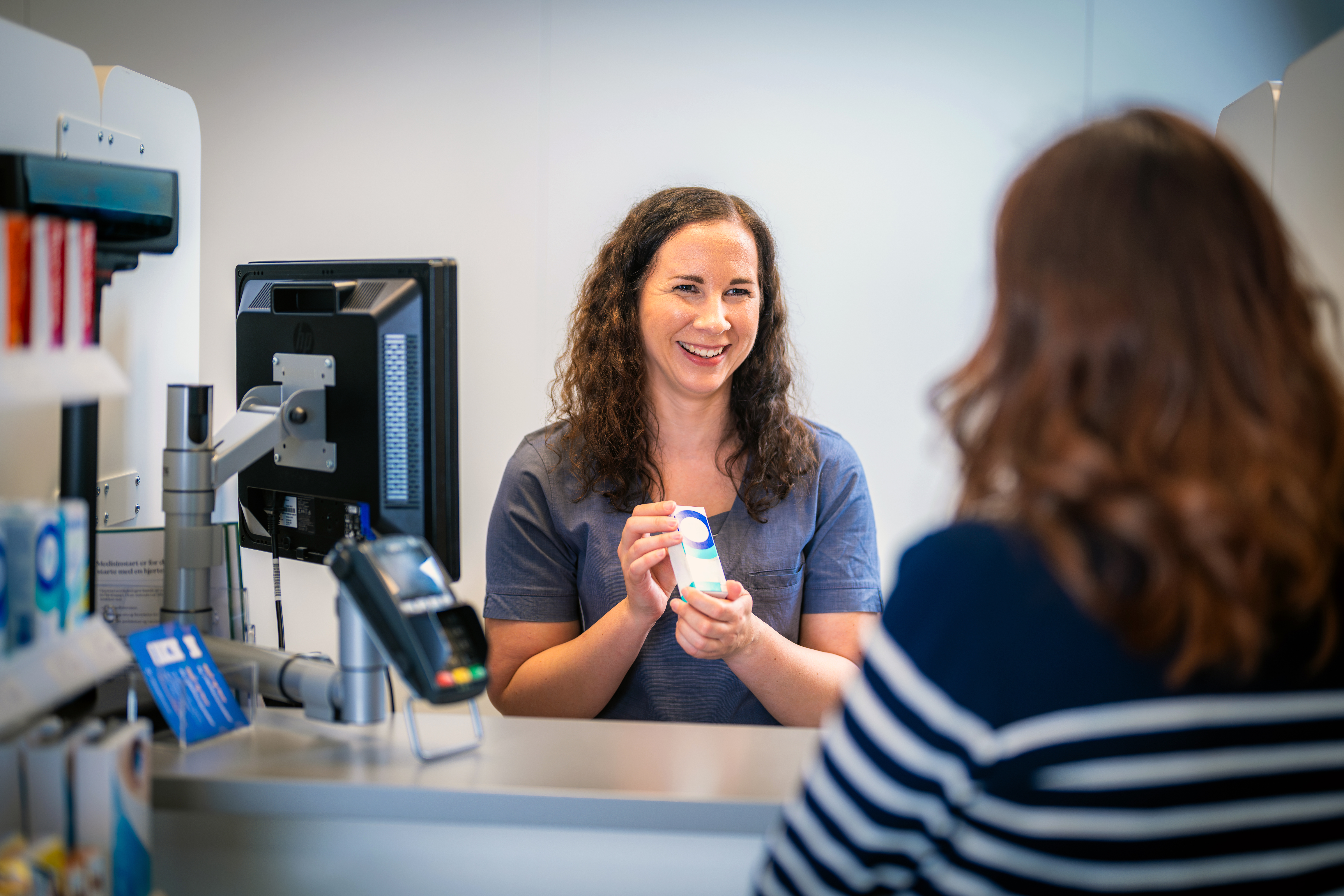 Farmasøyt som viser frem vare til kunde i kassen